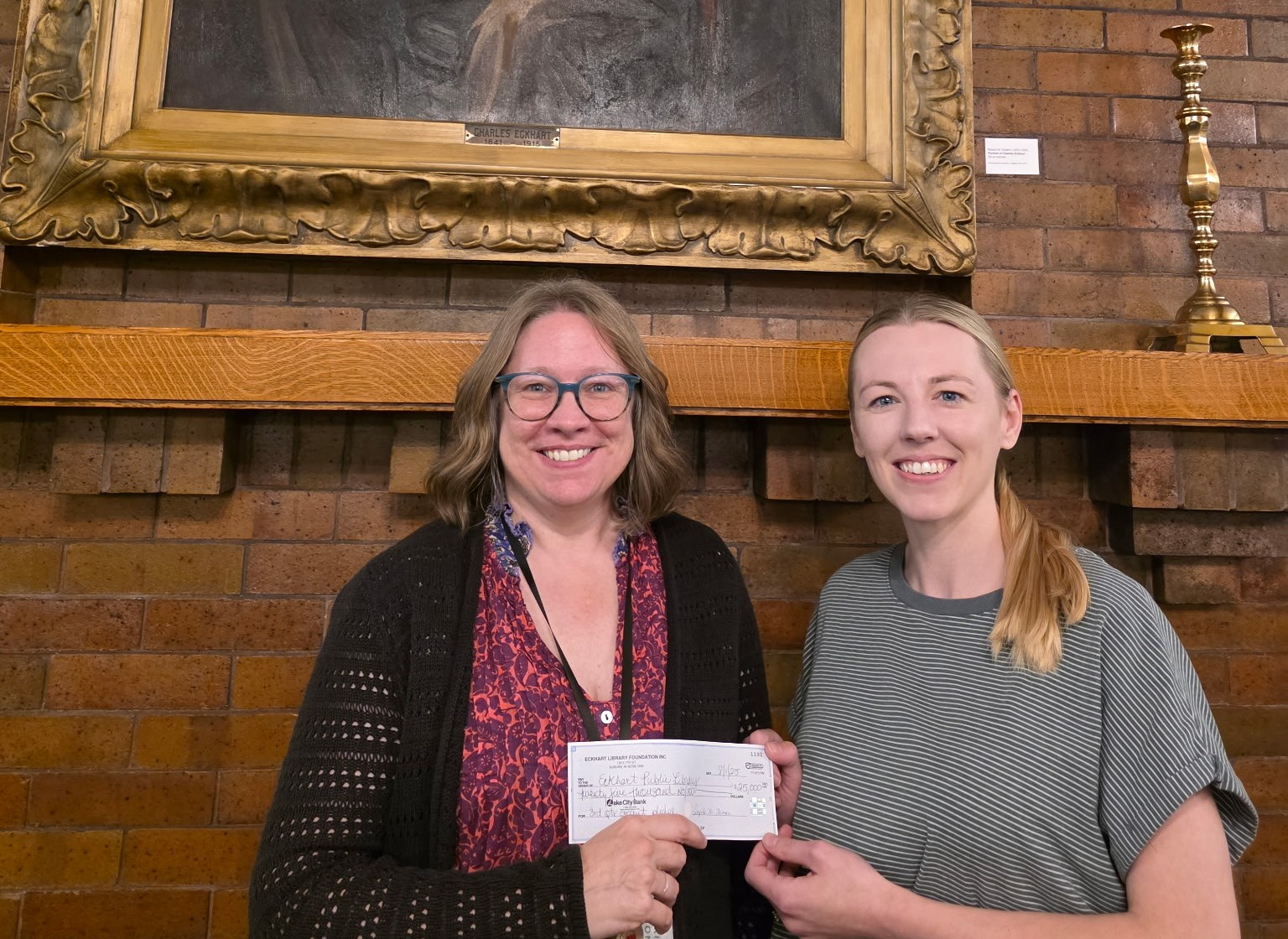 two ladies holding check in front of historic fireplace